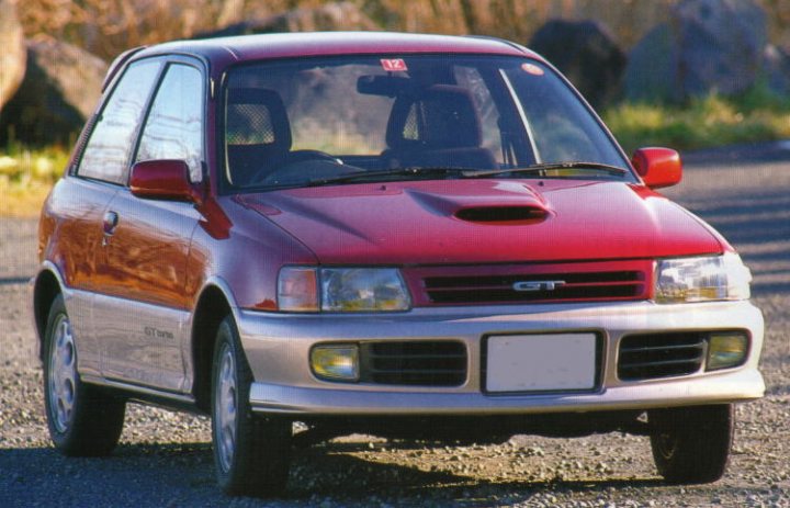 There must be a JDM car thats perfect for sprinting! - Page 1 - Jap Chat - PistonHeads - The image shows a close-up of a shiny red convertible car with a silver racing line stripe along its side. The car features a distinct hood scoop, black rims with white tires, and is parked on a rocky surface. It has two doors on the passenger side, and is captured from an angle that highlights its sleek design.