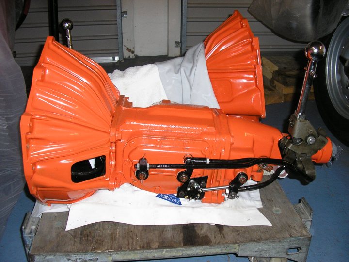 A piece of luggage sitting on top of a wooden floor - Pistonheads - The image shows an engine hoisted in an airplane hangar. The engine is predominantly orange with black accents, and it has five sections of ribbing across its front. It's attached to a pulley system with cables, which appears to be part of an assembly or installation process. The engine is set on a pallet, which is placed on the hangar floor. The setting suggests a workplace designed for the maintenance, repair, or construction of aircraft engines.