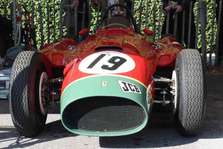 Revival images - Friday  - Page 1 - Goodwood Events - PistonHeads - The image depicts a vintage race car, prominently featuring a number 13 on its side. The car is a classic, red with green accents, and its position in the frame suggests it's on display at an event or museum. The surroundings imply an outdoor show setting, possibly near a vintage race car museum, as evidenced by the apparent fence and people in the background. The focus of the image is clearly the vehicle, with its historical design and unique charm drawing attention to the details of the car's engine, front fender, and the number 13 prominently displayed on its side.