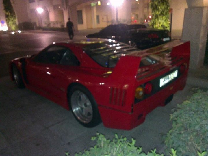 F40 Spotted - Marina Walk - Page 1 - Middle East - PistonHeads - The image depicts a vibrant and classic red convertible sports car parked in front of a building. There are wine glasses next to a short topless person. The car is equipped with a sunroof and is designed with a sleek and aerodynamic appearance. The license plate on the car reads "JlaAU". The setting suggests an evening moment, perhaps in a city or suburban environment.