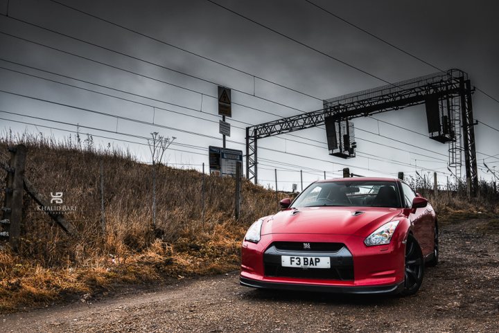 Pistonheads - The image captures a striking scene of a red sports car parked on a dirt road. The car, prominently bearing the license plate "F3 BAP", is positioned right in front of the frame, making it the embodiment of expressionism - vivid colors, power, and speed represented in the form of this vehicle. 

In the background, a wooden fence can be seen, partially obscuring the view of a railway track. Above the railway track, power lines crisscross the scene, adding a layer of complexity to the composition. 

The track, fence, and power lines create a sense of depth and scale, making the car appear even more eye-catching. The overall atmosphere suggests a sense of solitude and anticipation, as if the car is ready to roar and speed into oblivion.