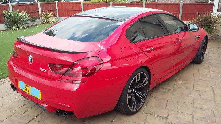 Just bought an M6 Gran Coupe - Page 33 - M Power - PistonHeads UK - The image shows a bright red sports car parked on what appears to be a driveway. The vehicle has a customized body kit, giving it a more aggressive and sporty look. The rear wing spoiler is prominent and suggests high-speed capability or racing pedigree. There's a visible license plate with the letters "K5Y". In the background, there's a glimpse of a residential area, including a fence and a portion of a building that resembles a church with a cross on top. The style of the image is a straightforward photograph with no filters or artistic manipulations.