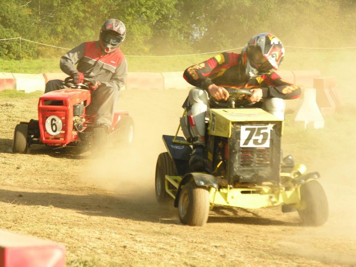 Racing Pistonheads Diary Midlife Lawnmower Crisis - In the image, two men are engaged in action on a dirt track. They are on all-terrain vehicles, which are covered in a layer of dust raised by their fun-filled activities. One man in the foreground accelerates past another man in the background, both armed with helmets for safety. The scene is blurred, indicating swift motion, and it appears to be a sunny day, enhancing the outdoor recreation theme. Their vehicles, the men, and the surrounding environment create an atmosphere of excitement and adventure.