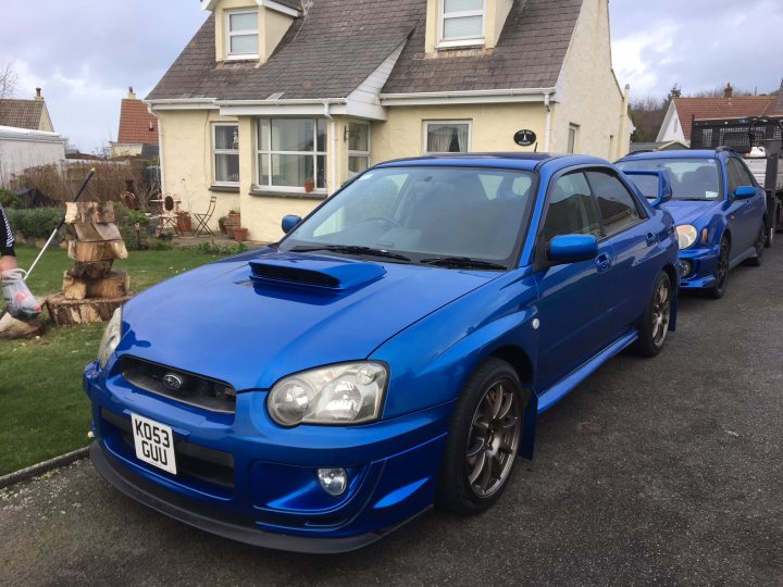 RE: Subaru Impreza WRX STI Type UK: PH Fleet - Page 3 - General Gassing - PistonHeads - The image shows a blue Subaru Impreza car parked on a street. It has been modified with aftermarket parts, including a large front bumper and a wide-body kit, which gives it a sporty appearance. The vehicle is in good condition, with a clean exterior, suggesting it may be well-maintained. In the background, there is a house, indicating that this is a residential area. There are no visible people or distinctive landmarks in the image, making the car the main focus of the scene.