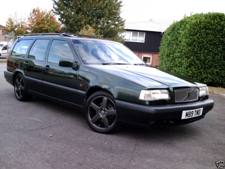 Original Loved Pistonheads Estates - The image features a black Volvo 740 estate parked on a driveway. It has silver rims, silver door handles, and a white license plate. The vehicle is parked facing the camera, and the backdrop includes some trees and a house. The car appears to be in good condition and is free of any visible damage.