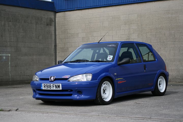 Any love for steel wheels? - Page 4 - General Gassing - PistonHeads - The image captures a side view of a blue Honda Fit compact car. The car is parked on a concrete surface next to a concrete wall, which is dotted with a few windows. The side of the car is the primary focus of the image, showcasing the car's sleek design and white wheels. The setting seems to be outdoors, with the car positioned as if it were ready to move or switch lanes on a road.