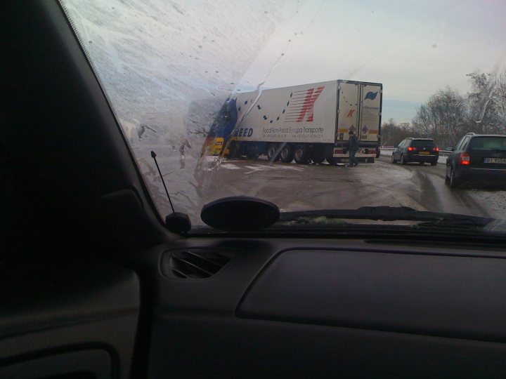 Pistonheads - The image captures a winter scene featuring a white and blue truck. Due to the angle and contrast, the truck appears somewhat distorted, with its dimensions seemingly shifted. The surroundings appear to be snowy and icy, indicating recent cold weather and possibly taking place on a highway or major road. There are other vehicles visible, moving in the same direction as the truck. The focus is on capturing the interaction between the landscaped and the truck.