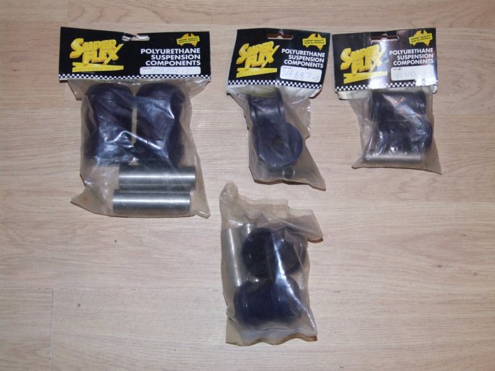 A pair of scissors sitting on top of a table - Pistonheads - The image shows four packages of car suspension components lying on a wooden floor. Each package contains a black suspension component alongside a small silver-colored cylinder, which appear to be suspension caps. The packages are sealed in plastic with the product details visible through the packaging.