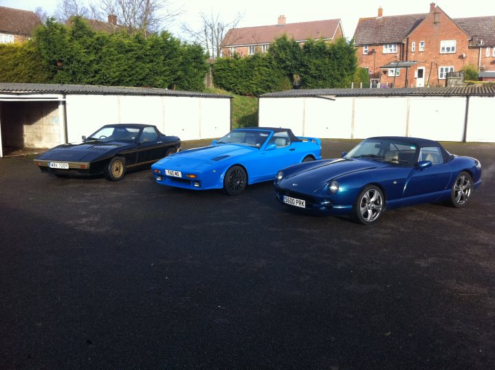 What? No Whats on in 2013!! - Page 2 - East Anglia - PistonHeads - The image showcases three classic drop-top sports cars parked in a lot, each a different color: blue, black, and red. They feature distinctive design elements such as large vents and a sweeping roofline. Their white-walled wheels add to their vintage charm. One door is opened, revealing the interior of the blue car. The cars are arranged side by side, with the blue one on the left and the black and red ones to the right. The setting is an outdoor paved lot with a clear sky, and the presence of brick buildings in the background suggests an urban environment.