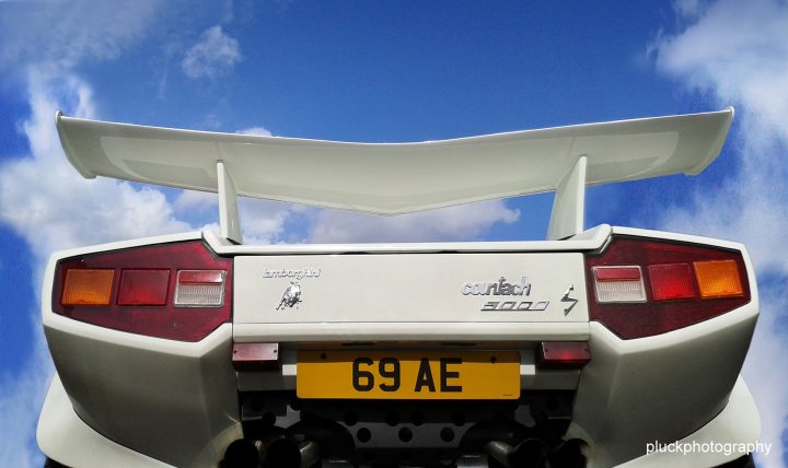 Countach  - Page 60 - Lamborghini Classics - PistonHeads - The image showcases the rear view of a white sports car. The car has a bright yellow license plate that stands out against the vehicle's white body. The car is situated against a backdrop of a blue sky, with wispy clouds adding depth to the scene. At the top of the picture, there is a banner with the text "Cluck Photography," likely indicating the photographer or studio that took the image.