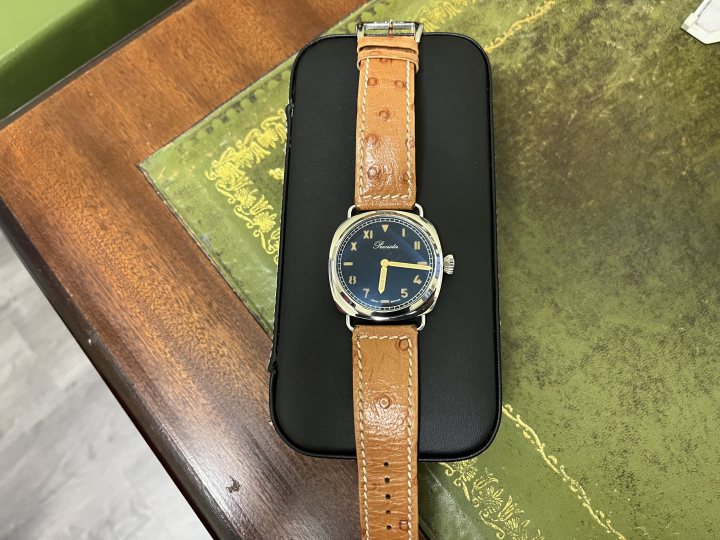 The OFFICIAL watches wanted/for sale thread - Page 3 - Watches - PistonHeads UK - The image showcases a smartphone case with an orange belt watch on it. The case and watch are placed on a table, suggesting they may be new or recently purchased items. The case is open, allowing the watch to be displayed prominently. In the background, there's a brown table that provides a simple, uncluttered backdrop for the main subjects. The overall composition of the image suggests it could be a product photo used in an online store or catalog.