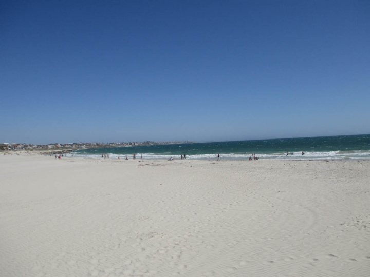 Landed a Month or so ago, how's it going? - Page 1 - Australia - PistonHeads - The image shows a sandy beach with a light tan color. The beach is vast and mostly empty, with a few people scattered along the shoreline. The ocean is a deep blue-green color, and there is a pristine view of the water. The sky above is a clear blue, indicating a sunny day. The horizon line is where the meets the sky, suggesting that the beach is close to the ocean's edge.