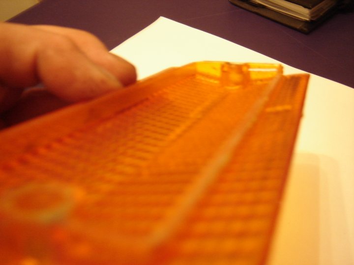 Lenses Pistonheads Indicator - The image features a close-up view of a? approx. 20 inches long, lying on a white surface. The orange color of the keyboard is striking. A hand holding a page is grabbing the top right edge of the Keyboard. The top left corner of the image shows a book in the background. The focus is on the keyboard, with the rest of the scene out of focus.