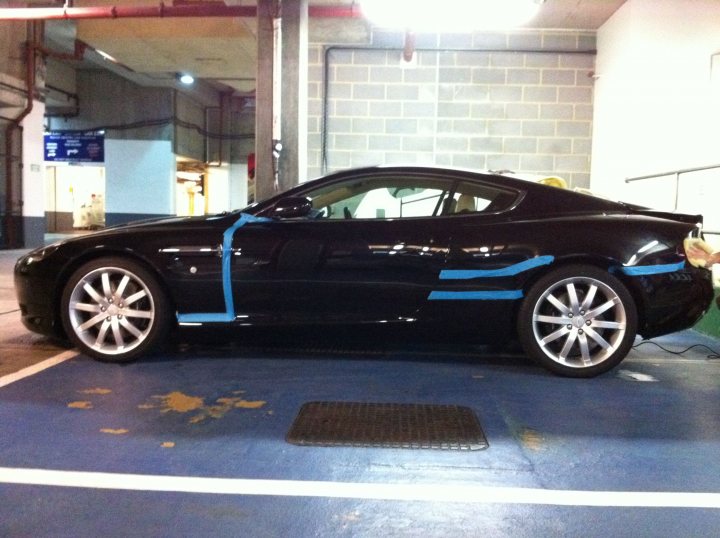 Pistonheads - In the image, a black sports car is parked in a large underground parking lot. The car has blue duct tape applied to its hood, possibly as a repair or as decoration. The vehicle is positioned on blue paint typically used to clearly mark spaces. The low ceiling and the dim lighting suggest that the car is in a multi-level parking facility, possibly a garage or a parking deck. There are no people visible in the image, giving it a calm and serene atmosphere.