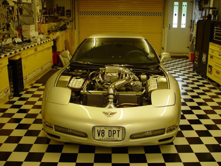 Pistonheads - The image showcases a sports car bay area of a garage. The car, a Corvette as indicated by the license plate, boasts a significant car mod that includes a large engine equipped with turbochargers. The engine is prominently on display, revealing its complex structure and metallic components. The garage is well-lit with fluorescent lights, and the floor is checkered black and white, typical of many garages or automotive workshops. This setting suggests an environment focused on mechanical work and automotive enthusiast culture.