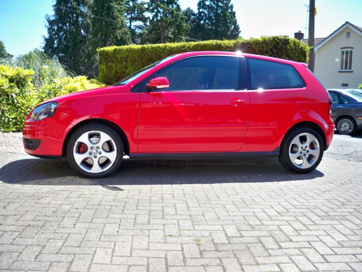 Gti Polo Pistonheads - The image shows a vibrant red Volkswagen Polo parked on a brick driveway. The sun is reflecting off the car and the driveway, creating a bright and cheerful atmosphere. The car is positioned in profile, allowing a clear view of its design features, including the narrow headlights and round taillights. Behind the car, there is a row of neatly trimmed bushes and a classic house with a driveway that runs alongside the house. The overall scene suggests a pleasant residential area.