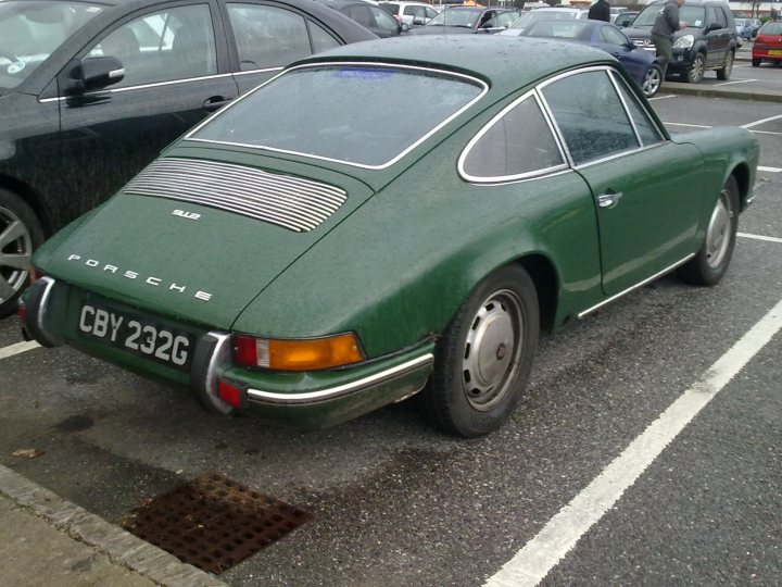 Pistonheads - In the image, a green Porsche car is parked in a parking lot. The car is positioned in the left lane, facing towards the right. It's a vintage model, judging by its design and color. The license plate of the car reads "CBY 232G". The parking lot appears to be quite busy, as there are other cars and a truck visible in the background. The ground is made of asphalt, featuring clearly marked lanes for parking.