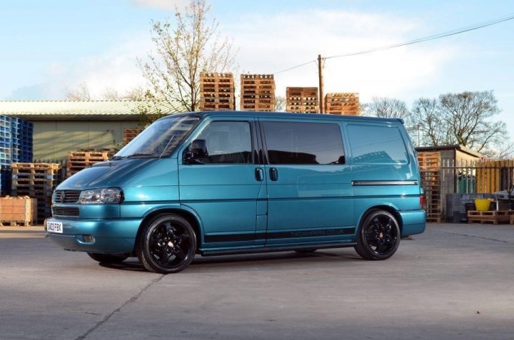 First T5 Camper - Page 1 - Tents, Caravans & Motorhomes - PistonHeads - The image presents a scene of a light blue Volkswagen van parked at a storage facility. The van has black rims and a compact design, which is characteristic of VW cargo vans. It's currently on what appears to be a concrete or tarmac ground surface. The background scene reveals brown wooden pallets stacked in piles, indicating this place might be used for storage, perhaps for goods transportation. There is also a clear sky visible, suggesting it's during the daytime under fair weather conditions.