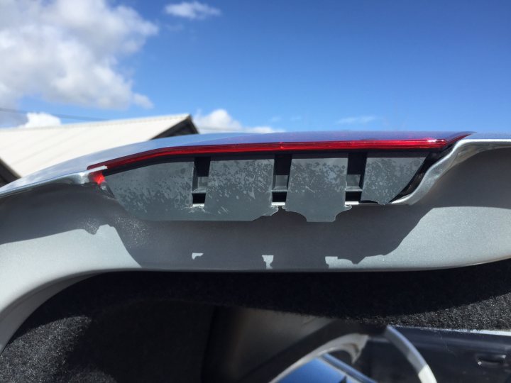 A close up of a car on a motorcycle - Pistonheads - The image presents a close-up view of the trunk release button on the back of a BMW vehicle. The button and its plastic bumper are in focus, while the rest of the car is only partially visible in the background. The button, appearing large and with a shiny, metallic surface, is attached to a black cloth panel, commonly used for coverings. The background, though blurred, shows a hint of a cloudy sky and the top of a house, suggesting that the vehicle is parked in a driveway.