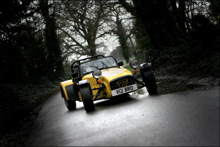 Back in April... - Page 1 - Caterham - PistonHeads - This image captures a scene of a yellow quad bike cautiously driving down a narrow, dirt road. The quad bike, with its distinctive four-wheeled design, is the most prominent object in the image, taking up a large portion of the space. The road itself appears to be wet, suggesting recent rain, and it's surrounded by lush greenery. On either side of the road, bare trees with no leaves intertwined with the foliage can be seen, giving the path a cozy, secluded feel.