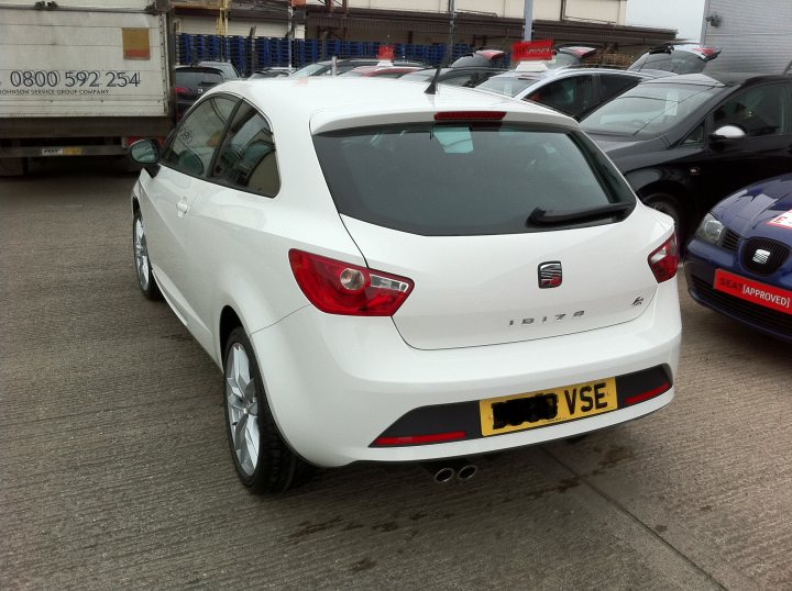 Seat Ibiza Tdi Pistonheads - This image presents a scene in a parking lot. At the forefront, there is a white hatchback car parked diagonally with its front on the left. The car is shiny and relatively new, with a visible license plate. It is positioned in front of a larger vehicle, possibly a truck or a van. The vehicle in the foreground casts a slight shadow, indicating that the sun is not directly overhead in the image. In the background, there are additional vehicles parked, creating a layered and populated parking area.