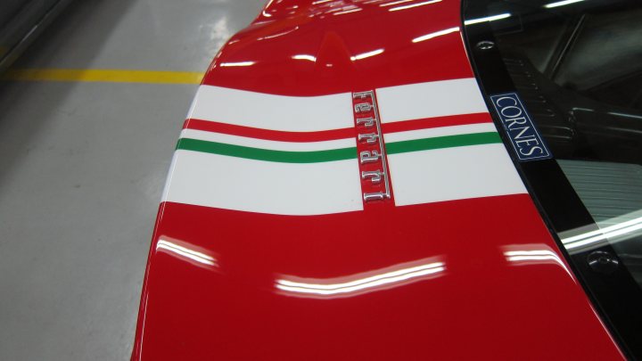 garage to service 360CS? - Page 1 - Middle East - PistonHeads - The image shows a close-up view of a custom-painted body part. Most of the visible surface is a vibrant red color, with a wide white stripe in the center featuring four green stripes arranged in a diagonal pattern. The style of the painting includes a reflective finish, giving the surface a smooth and polished appearance. The bottom edge of the image appears to be the metallic surface of a workplace or workshop, possibly a garage, as indicated by the presence of a stripe that marks a safe or boundary area. The quality of the paintwork is high, suggesting this could be a vehicle from a racing team or a high-end modification in a custom automotive setting.