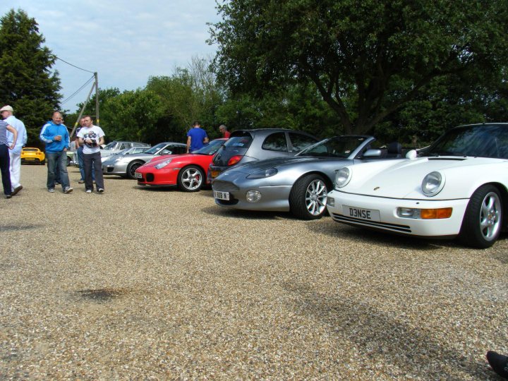 Breakfast Meeting, The Hare, Roxwell 4th June - Page 1 - Kent & Essex - PistonHeads - The image depicts a gathering of people in an open field, standing near and between various classic cars. The cars are parked on a gravel or dirt surface, and their variety and conditions suggest they may be vintage or something similar. There appear to be multiple individuals present, engaging in conversation with each other and observing the vehicles. The setting is outdoors, under a partly cloudy sky, and the ground is covered in small stone fragments, indicating a rustic or rural location. There's a casual, social atmosphere evident in the gathering, as people appreciate the collection of classic cars.