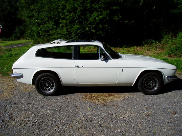 Pistonheads - The image shows a classic white two-door car parked on a gravel surface. The car is an older model, characterized by its round headlights and a small roof spoiler. The surrounding environment includes a grassy area with trees near the car, suggesting a park setting. The sky visible in the top left corner of the image appears to be overcast. The car is oriented towards the left side of the image, with its front facing the viewer and its rear facing a path that seems to lead deeper into the natural surroundings. There are no visible texts or distinctive markings on the car or within the image. The style of the photograph is candid, likely taken to document the presence and condition of the vehicle in this outdoor space.