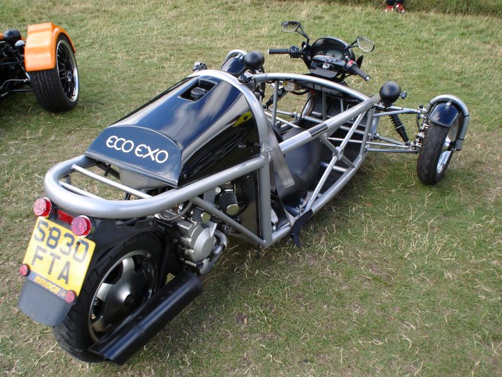 Pistonheads Exoeco Mev - The image showcases a three-wheeled motorcycle parked on a grassy field. This unique vehicle has a low-carriage design, which is accented by a blue and black body color. The motorcycle features an eggy washing machine-style design, adding a touch of whimsy to its overall appearance.