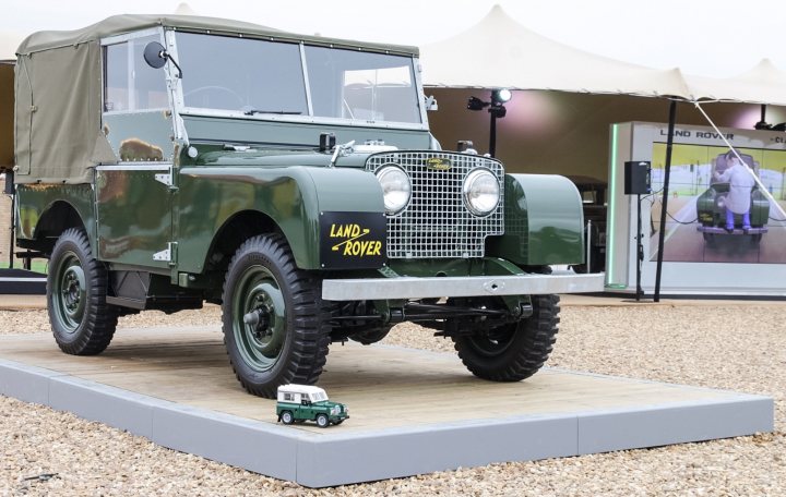 RE: Lego Land Rover project - Page 3 - General Gassing - PistonHeads - In the image, there's a display of the Land Rover car brand. The main focus is a large, robust green jeep, likely a replica or an older model, occupying most of the frame. In the background, a small, toy-like jeep is placed to show scale, sitting proportionally behind the larger vehicle. The setting appears to be a convention or an expo, with the ground covering a fabric floor, possibly made of metal, used as a stage-like platform for the display. The environment suggests the event is meant for informative or promotional purposes, showcasing automotive history and design.