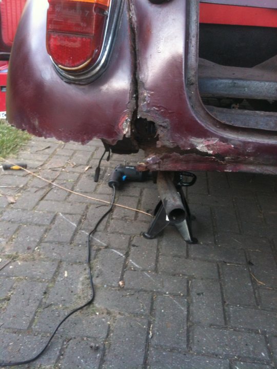 1971 Morris Minor 1000 Resto thread (Maybe) - Page 1 - Classic Cars and Yesterday's Heroes - PistonHeads - The image shows the rear view section of a car with a significant amount of damage. The paint on the fender is severely chipped and peeled, exposing the underlying metal. A spite weld is improvised, adding to the distressed appearance of the vehicle. The damage suggests a collision has occurred. The photo captures the condition of the vehicle in a close-up shot, focusing on the affected area of the car.