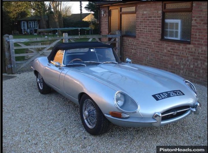 Replica E-Types: why undervalued/underappreciated? - Page 2 - Kit Cars - PistonHeads - The image features a striking silver sports car parked on a gravel driveway. The car is positioned facing the camera, revealing its clean and well-maintained design. A distinctive license plate, "DAP238," is prominently displayed on the back. Surrounding the car are pedestrian-friendly flagstone pathways, and in the background, there is a quaint brick cottage, adding to the picturesque setting. Above all, a sense of tranquility and elegance is depicted in this scene.