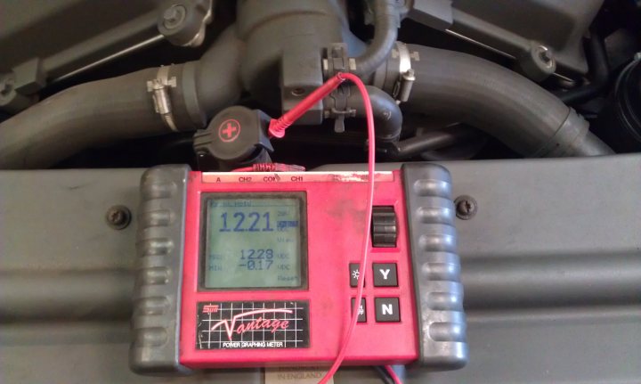 Flat battery - OK to jump start? - Page 1 - Aston Martin - PistonHeads - This image captures a close-up view of a red device with a digital display, connected to an engine using red cables. The device is sitting on the metal surface of a vehicle, likely for engine diagnostics or reading. The digital display shows several readings, indicating metrics of the vehicle's operation. The word "Vintage" is visible on the device, which might be the brand or model of the device. The engine beneath it is fully visible, highlighting the complexity of the vehicle's internal workings.