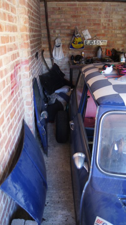 Is it worth anything?? - Page 1 - Classic Minis - PistonHeads - The image presents a vintage scene inside a brick shed attached to a large vehicle, possibly a train. The inside of the shed appears cluttered, suggesting it's used for storage. On the brick wall, a bit of graffiti is visible, adding a sense of abandonment or perhaps nostalgia. A few recycling symbols are depicted, indicating an interest in recycling or eco-consciousness. A damaged blue wing mirror is hanging off the door of the vintage car outside the shed, adding to the overall vintage feel of the scene.