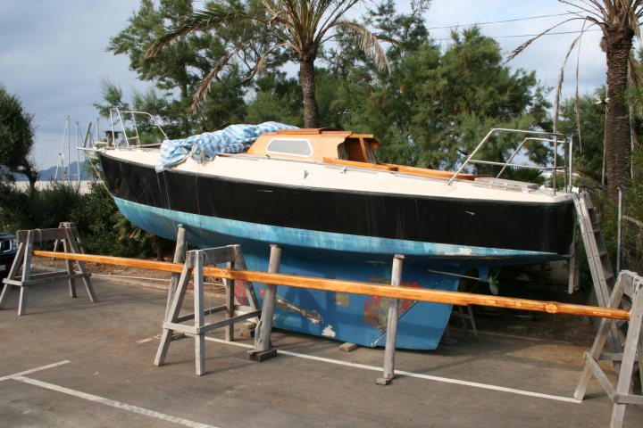 Roll on Summer...Boat Pic's, let see them... - Page 3 - Boats, Planes & Trains - PistonHeads - The image displays a brown boat adorned in blue and white, presumably at a marina given the presence of a wooden railing, with the scenic backdrop of palm trees undoubtedly adding a tropical touch to the picture. The boat is unique due to its prominent retro Allibard design. It appears to be stationary in a storage area, possibly undergoing maintenance or simply waiting for its next voyage. The overall scene is serene and picturesque, indicating a quiet day at the marina.