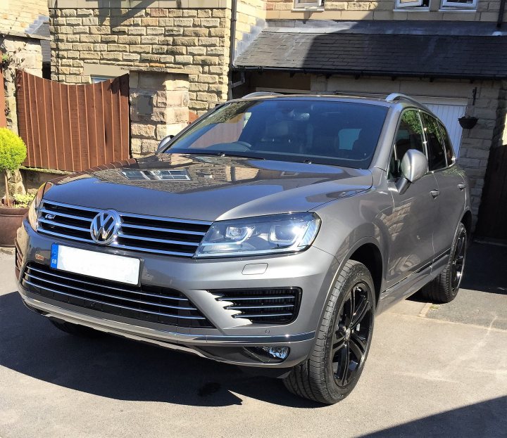 2017 VW Touareg R Line Plus - Page 1 - Readers' Cars - PistonHeads - This image depicts a silver Volkswagen car parked on a residential driveway. The car has a sleek design with black rims, and the license plate is clearly visible on the front of the vehicle. In the background, there is a brick building partially visible and a potted plant to the left side of the frame. The driveway appears to be paved and the car is angled towards the camera from a three-quarter side view. The image is taken during daylight, and the car appears to be in pristine condition.