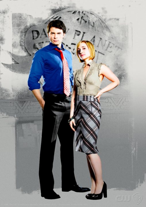 Chloe Smallville Clark - This is a posed promotional image featuring a man and a woman standing close to each other. The woman is positioned slightly behind the man, slightly to his right, and she is wearing a skirt and heels. She has short blonde hair and is looking directly ahead with a slight smile. The man is dressed in a blue shirt, gray pants, and a red tie, and he also has short dark hair. He is looking directly at the camera with a neutral expression. Both individuals are facing forwards, and there is paint splattering or a weathered background effect around them.