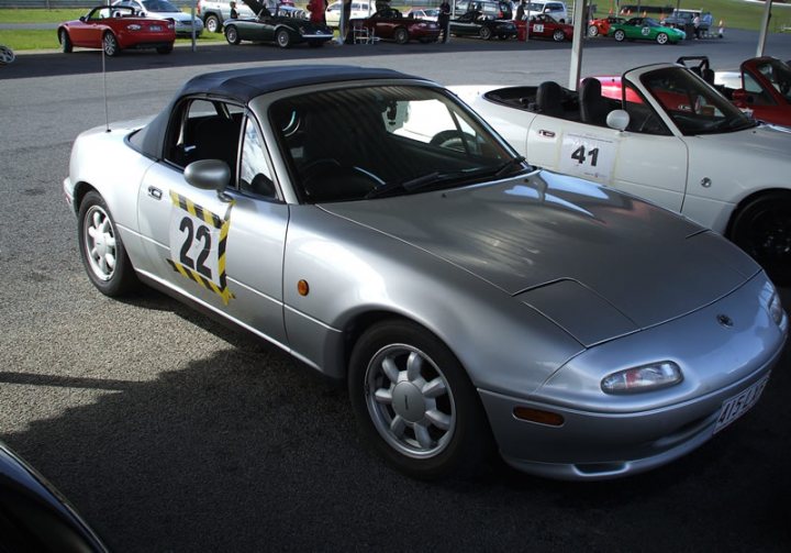 Pistonheads Sort Warpaint - The image features a silver sports car parked in a lot, characterized by its smooth lines and distinctive black and yellow numbers "22" across its hood. The car's sleek design is highlighted by a shiny surface, and it's positioned next to a white sports car, suggesting an event or showcase where different models are on display. The lot is filled with various cars and a few people who might be attendees or enthusiasts, adding to the dynamic atmosphere of the scene. The background is not highly detailed, giving the spotlight to the silver sports car and its surrounding vehicles and people.