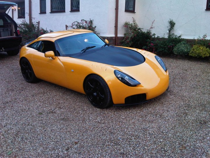 Pistonheads - The image features a bright yellow residential setting with a unique sports car parked in a gravel driveway. The sports car is characterized by its low and wide design, indicating it's likely a mid-engine model with a removable roof. The car is backed into the parking spot, facing the opposite direction of the typically presumed direction in American parking. This black and white photograph highlights the vehicle's vibrant color and the immaculate residential backdrop.