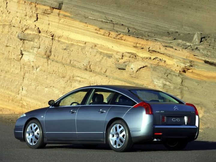 Any modern cars that will be a classic in years to come?  - Page 1 - General Gassing - PistonHeads - The image shows a silver-colored sedan parked next to a steep, eroded cliff face. The vehicle has a badge that reads "C6" on its trunk and appears to be parked on an asphalt surface. Below the car, the ground is mostly in shadow, suggesting that the photo was taken during the day. The contrast between the car and the natural background is striking, highlighting the sleek and modern design of the vehicle.