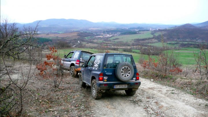 Couple of pics from today... - Page 1 - Off Road - PistonHeads - The image shows a rustic outdoor setting featuring two Suzuki sports utility vehicles on a trail. The vehicles are surrounded by dry grass and mountains, suggesting a high-altitude or remote location. The terrain is rugged and appears to be a dirt trail. It seems to be a misty morning given the overcast sky. The back windows of one vehicle are emblazoned with tribal-style tattoos, adding a unique touch to the image. The Suzuki branding is clear, indicating the model and make of the vehicles.