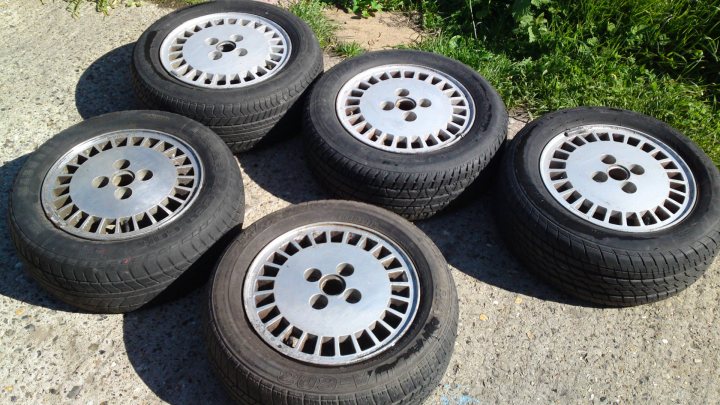 A close up of a bunch of different items - Pistonheads - This is a photograph of nine used car tires. Six of these tires have the same pattern of radial ridges extending from the hub element toward the outer edge. Three of the tires, however, exhibit a distinct design that consists of rings around the hub element followed by an equally spaced, radial pattern. The tires are stacked on a concrete surface with patchy grass edges.