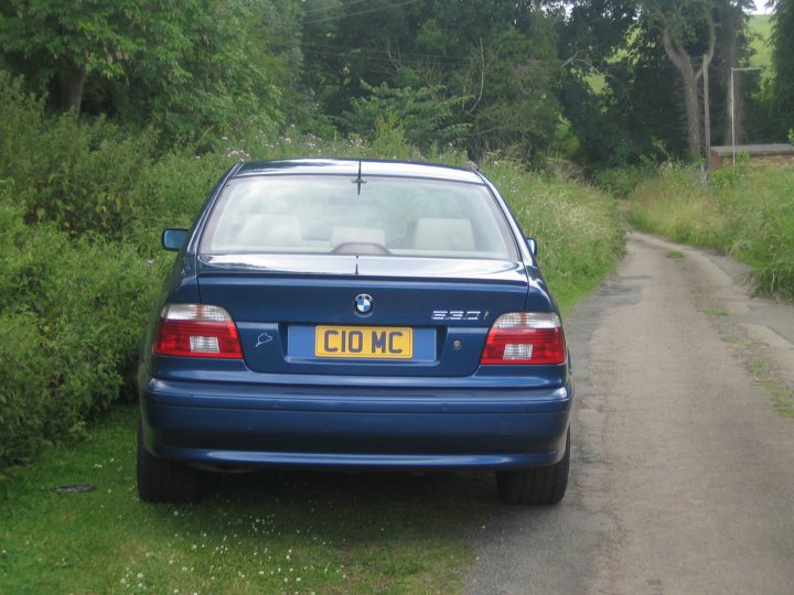Pistonheads Barge Bmw - The image portrays a serene rural scene featuring a blue BMW car parked by the side of a dirt road. The car is identified by its license plate, which reads "CIO MOW." The road itself is narrow, indicative of the countryside environment, and is neatly bordered by a grassy embankment on one side. In the distance, a trimmed hedge can be seen, suggesting some level of human tending to the landscape. The overall lighting of the photo implies an overcast day.