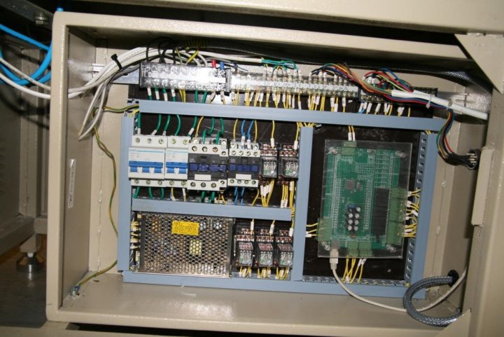 Any Electrical Engineers around? - Page 1 - Science! - PistonHeads - The image displays an open panel, likely a part of an electronic system, showing a complex array of circuit boards, components, and wires. The electronics consist of multiple printed circuit boards (PCBs) that look neatly organized, and various colored wires are connected to the PCBs. The components range from those that appear to be integrated circuits to what appear to be resistors or small inductors. The background is mostly dark, with certain areas illuminated by possibly UV or fluorescent lighting, emphasizing the panel's contents. The overall impression is of a tightly packed, professional, and technical environment, possibly within a server rack, subpanel, or similar industrial setting.