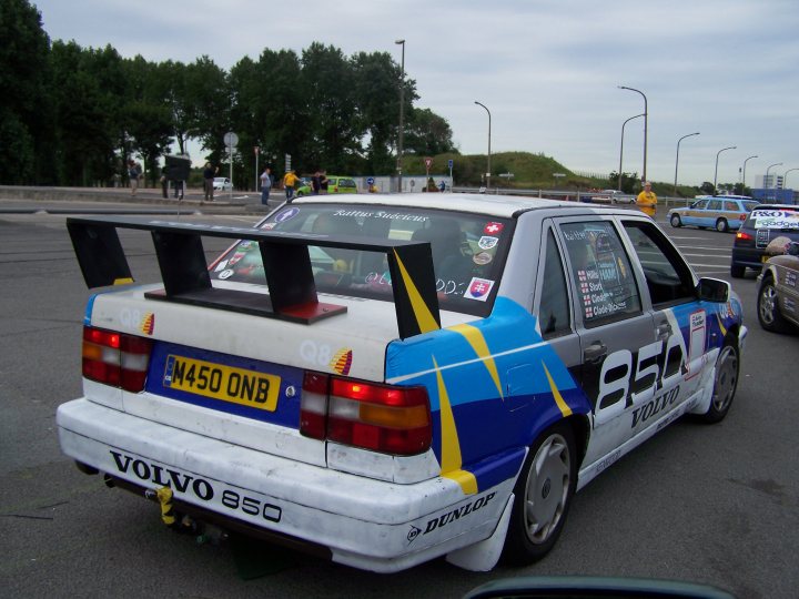 Best of the Bargain Basement Vol. 2 - Page 250 - General Gassing - PistonHeads - This image captures a white Volkswagen car parked in a parking lot. The car is easily recognizable with its distinctive rear wing painted in black, yellow, white, and blue colors. The license plate is clearly visible and reads "M450 ONB". The side of the car is adorned with various stickers, one of which is a small blue and white sticker with a number on it. In the background, there are trees and the upper edges of other parked cars can be seen, suggesting a popular parking area around historical buildings.