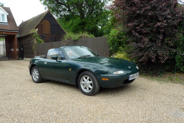 Pistonheads Mazda - The image showcases a vibrant green Porsche Boxster model, circa 1998, parked on a gravel driveway. The car, which is characterized by its two-seater convertible design, is facing towards the right and slightly towards us, the viewers. The setting includes a sturdy brick house and a large tree, both of which are partially obscured by the vehicle. The overall scene suggests a serene suburban neighborhood.