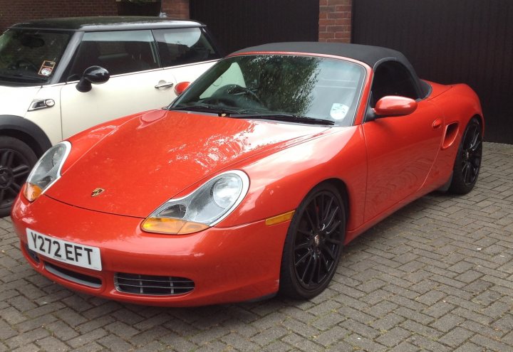 Do all cars look worse with black wheels? - Page 16 - General Gassing - PistonHeads - The image showcases a vibrant red Porsche sports car parked on a brick driveway. The Porsche is sleek and shiny, with a soft-top convertible roof. Its white license plate is clearly visible to the right. Across from the Porsche, there is another car, however, it is less prominent in the scene. The cars appear to be parked and stationary. The setting suggests a calm, possibly suburban environment with a residential driveway.