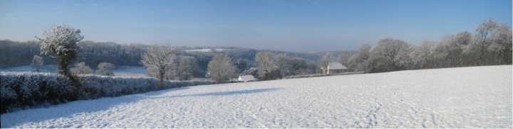 A person riding skis down a snow covered slope - Pistonheads - The image features a serene winter landscape where a large snow-covered field stretches out towards the horizon. The sky overhead is a deep blue, suggesting dusk or dawn, which adds a peaceful and mysterious ambiance to the scene. The field is marked by scattered trees, some of which are also blanketed in snow, enhancing the wintry atmosphere. In the distance, a small structure can be seen, possibly a house or barn, which adds a sense of scale and contrasts with the vastness of the snowy field. The image captures the calm and quiet before dawn or after dusk, as evidenced by the soft, diffused light.