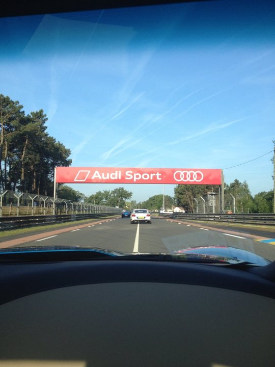 Stonking drive out - Sunday 14th - Page 7 - Yorkshire - PistonHeads - This is a photograph taken from the perspective of the driver's seat in a car, showing the windshield with a red promotional banner that reads "AUDI SPORT" displaying a car from behind. The windshield also indicates above the banner, in a more subdued red, the word "AUDI." Below the banner, the track itself is visible, with a few trees lining the circuit and another car approaching in the distance, though it's not in focus. The banner suggests advertising or event signage.