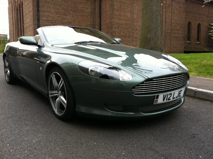 Lower front grille - Page 1 - Aston Martin - PistonHeads - The image shows a green Aston Martin sports car parked on a street by a brick building. The car is facing towards the left side of the photo, angled slightly to the right. The design and iconic branding suggest a high-end, luxury vehicle. The setting appears to be residential or city street, with the car occupying a significant portion of the frame.